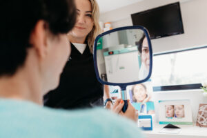Nurse prescriber Anna Lee with a client who is looking at her face in a hand mirror during a consultation at Exthetics, Exeter