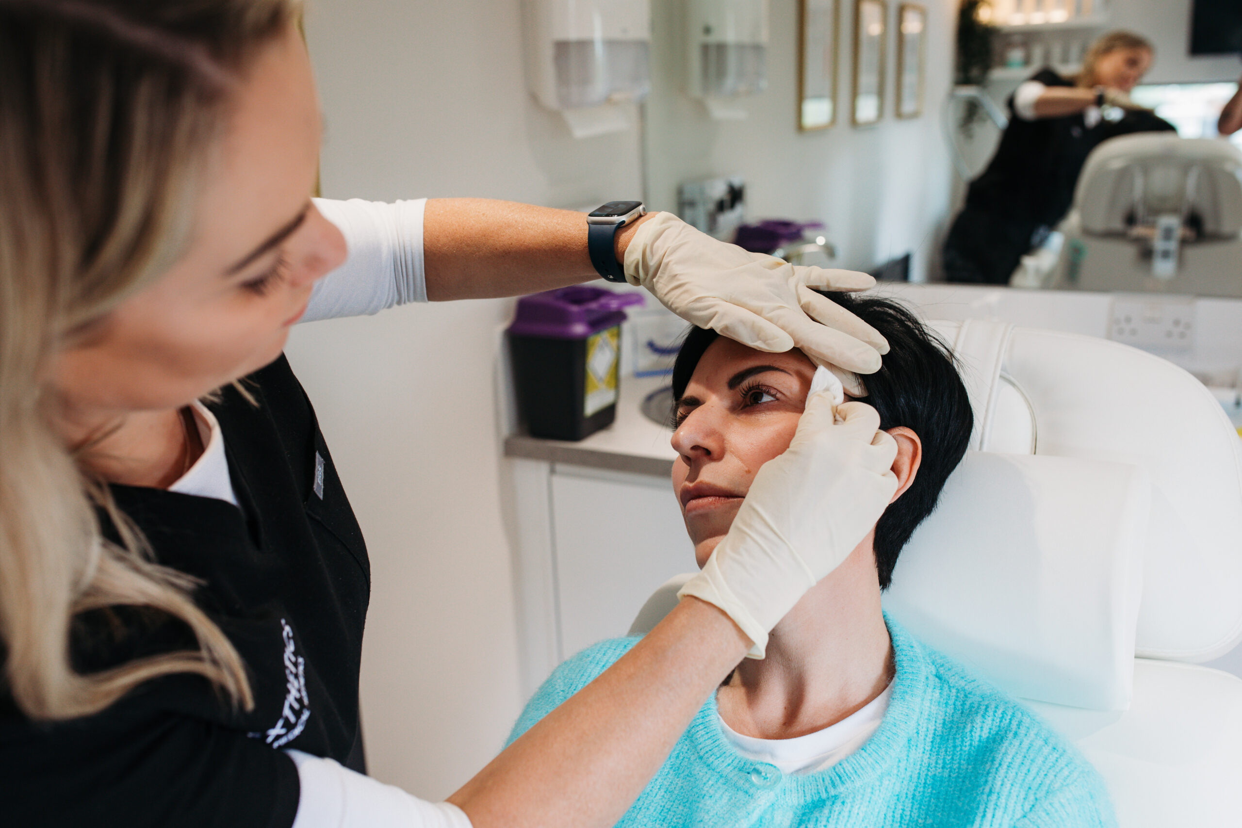 Anna Lee assessing a client's face with gloved hands before recommending any aesthetic treatment